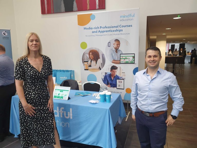 Two Mindful Education employees standing in front of a Mindful Education branded stand at an Industry event.