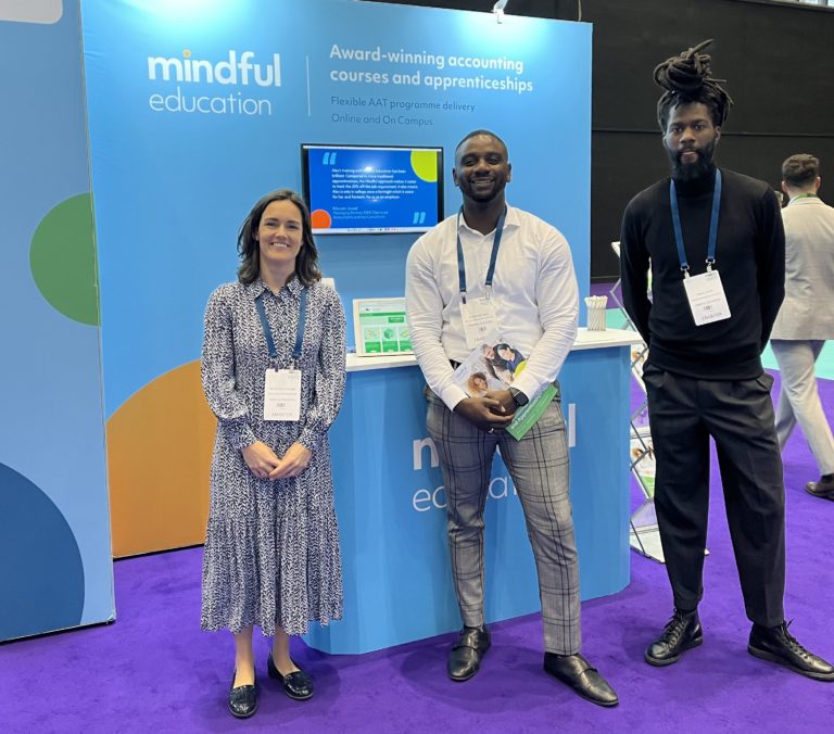 Three Mindful Education employees standing in front of a Mindful Education branded stand at an Industry event.