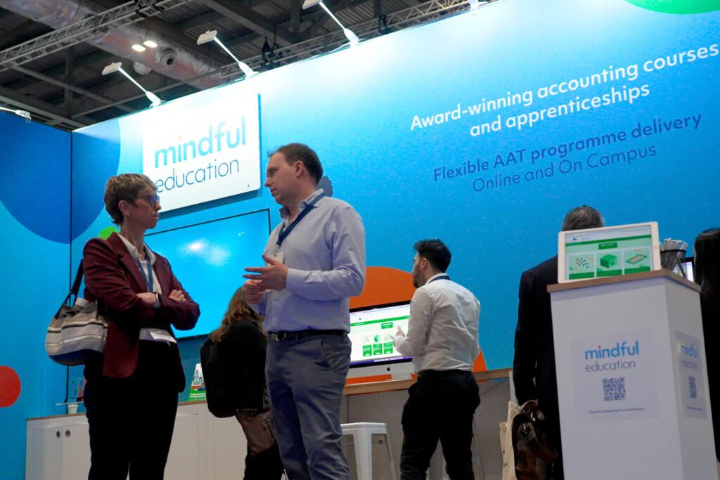 An image showing Mindful Education's stand at an industry event, with many people speaking to various members of the team about blended learning courses and apprenticeships.