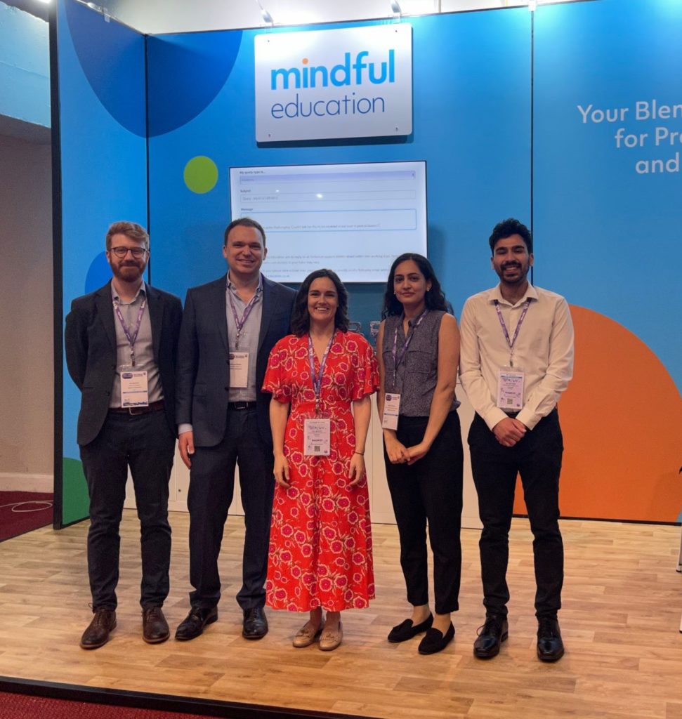 Five Mindful Education employees standing in front of a Mindful Education branded stand at an industry event.