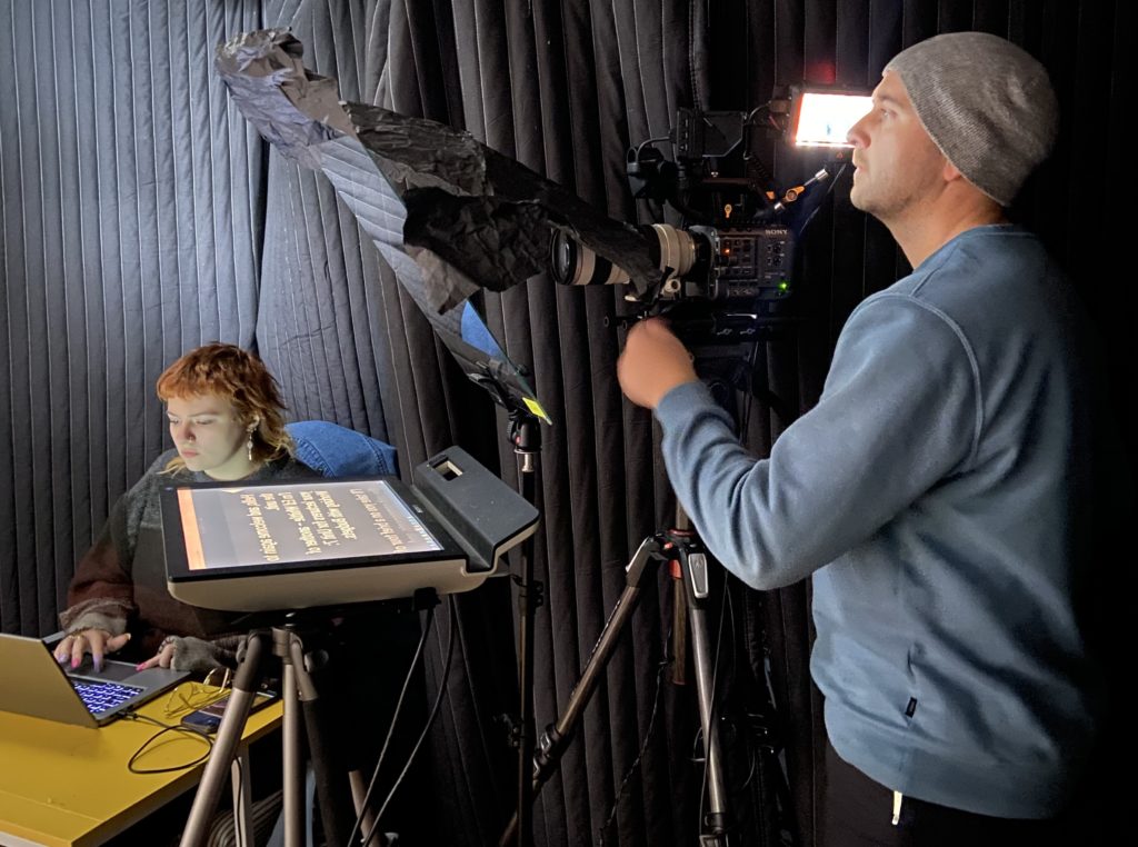 Two members of the Mindful Education production team in a studio, showing one checking a large camera and another using a laptop.