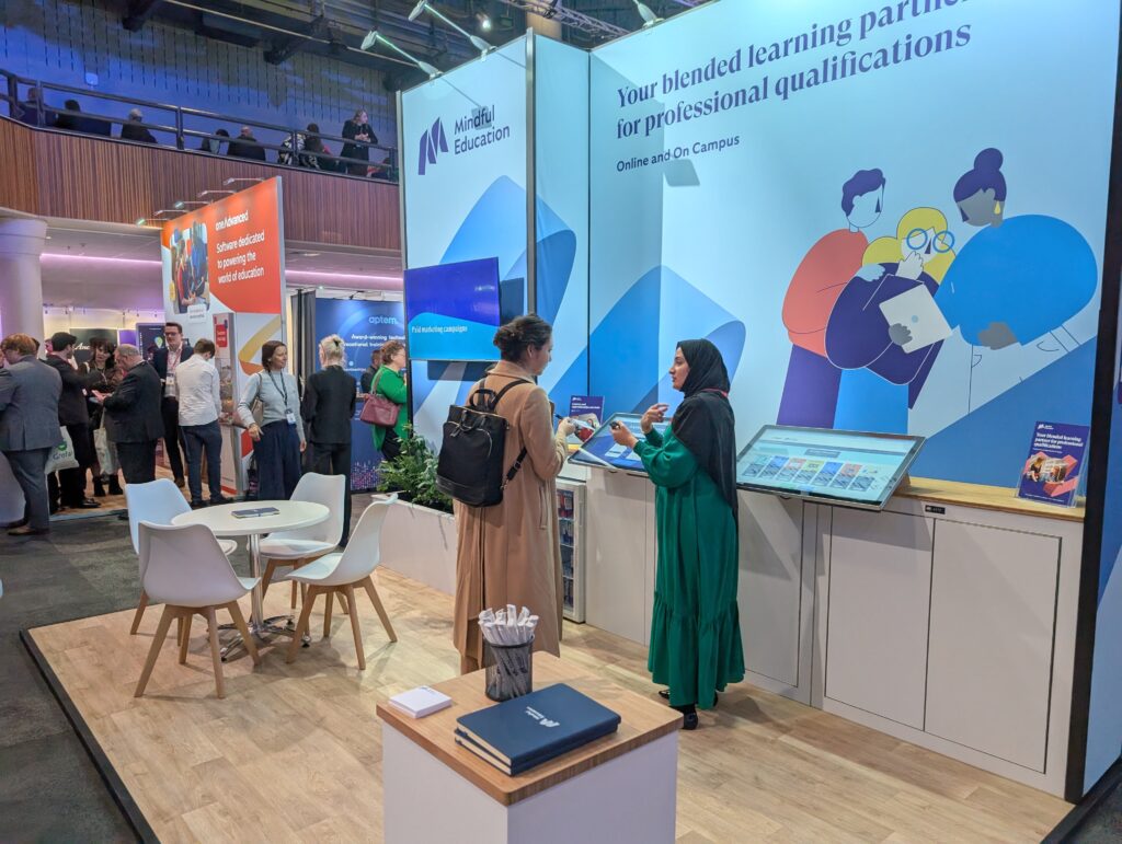 A Mindful Education employee at an industry event speaking to a delegate about Mindful Education's selection of flexible, part-time courses.