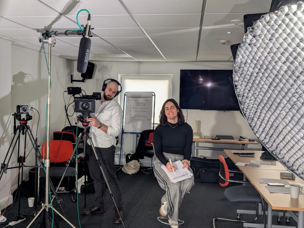 Two Mindful Education employees sitting amongst filming equipment and smiling at a camera.