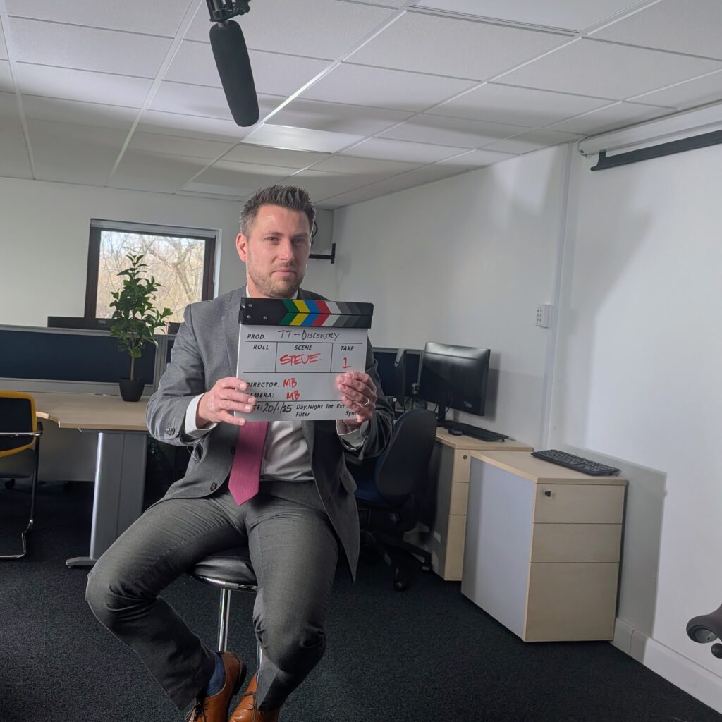 A finance director holding a clapperboard in front of filming equipment.