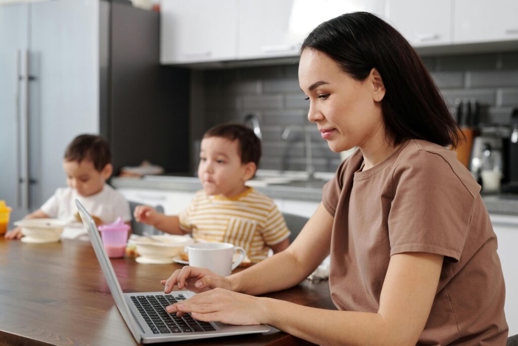 An image showing a parent working on their laptop, alongside her children, showcasing the flexibility of the blended learning model.
